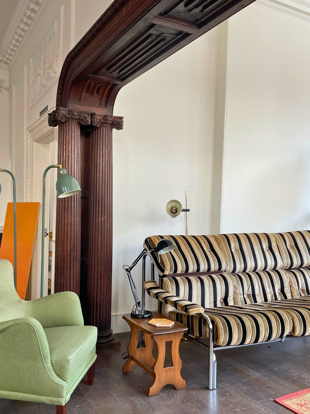 Living room with a green armchair, striped sofa, and wooden side table.