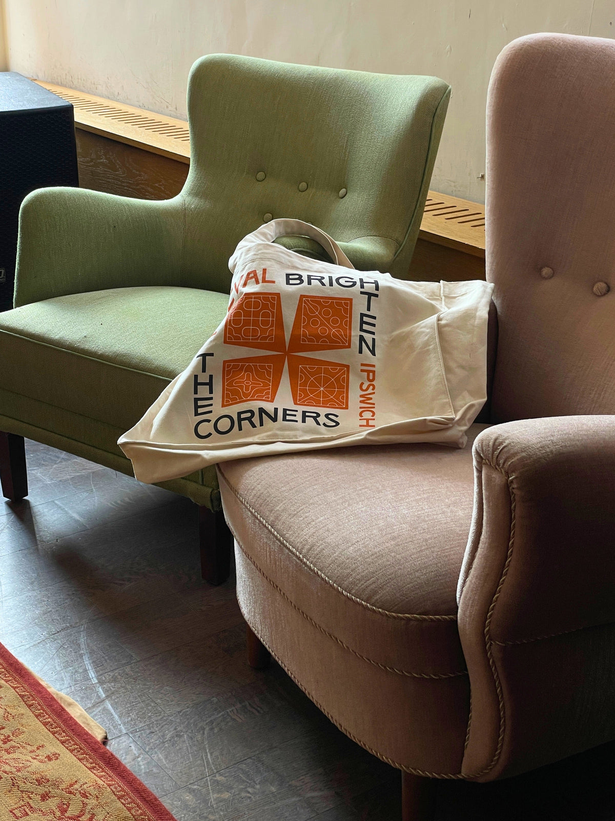 Dusty Pink armchair with a white tote bag featuring orange text and graphics on